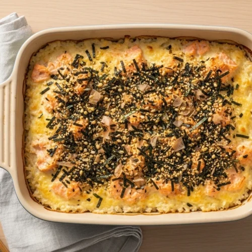 Easy and delicious salmon sushi bake in a ceramic dish with golden topping and furikake.
